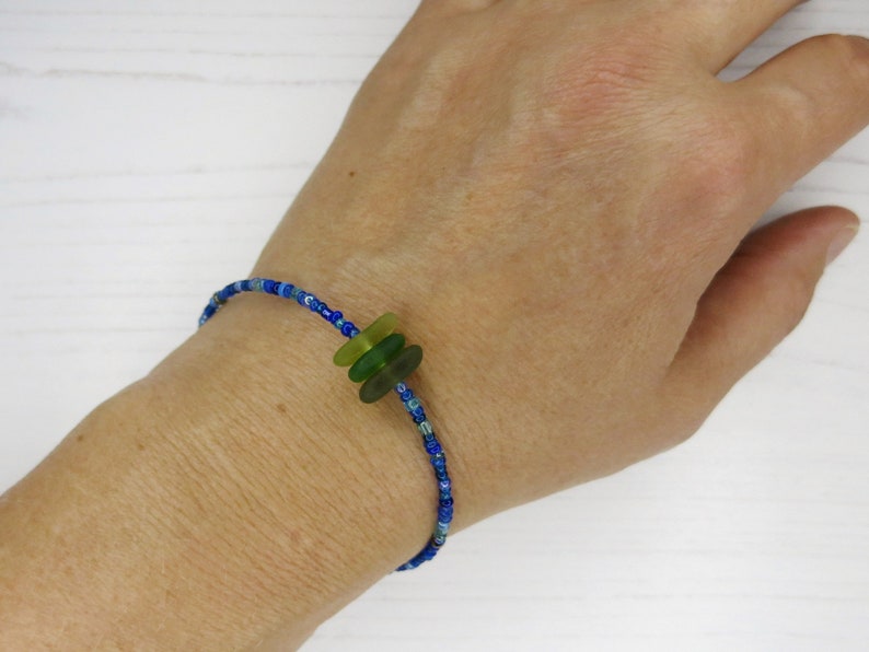 Dainty bracelet with three pieces of Cornish sea glass surrounded by tiny blue glass beads and fastened with a silver plated lobster catch photographed being worn.