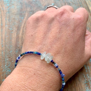 Dainty bracelet with three pieces of Cornish sea glass surrounded by tiny blue glass beads and fastened with a silver plated lobster catch photographed being worn.