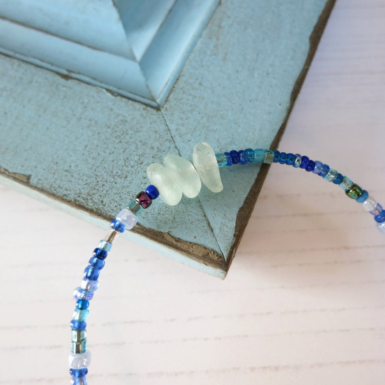 Close up of dainty bracelet with three pieces of Cornish sea glass surrounded by tiny blue glass beads and fastened with a silver plated lobster catch.