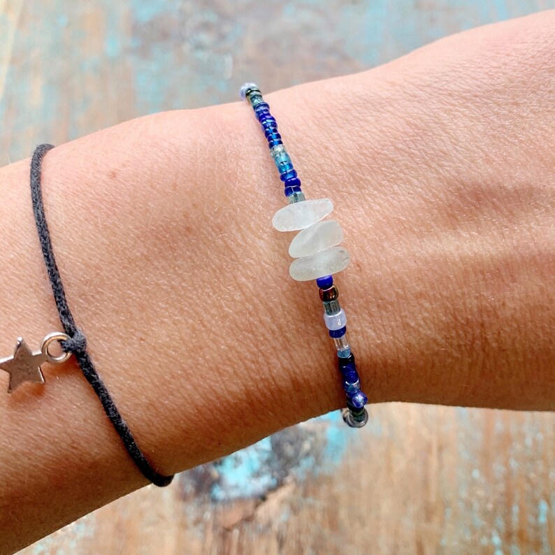 Dainty bracelet with three pieces of Cornish sea glass surrounded by tiny blue glass beads and fastened with a silver plated lobster catch photographed being worn.
