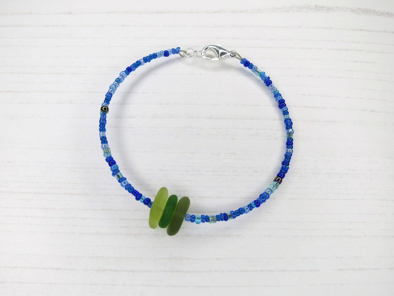 Dainty bracelet with three pieces of Cornish sea glass in shades of green surrounded by tiny blue glass beads and fastened with a silver plated lobster catch.