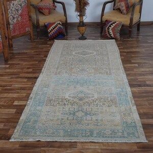 May include: A rectangular area rug featuring a faded, distressed pattern in shades of beige, light blue, and cream. The rug displays intricate geometric and floral motifs throughout its surface, with a distinct border and a central medallion design.