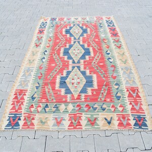 May include: A traditional Turkish kilim rug with a geometric pattern in shades of red, blue, green, and beige. The rug has a rectangular shape and is woven with a variety of textures.