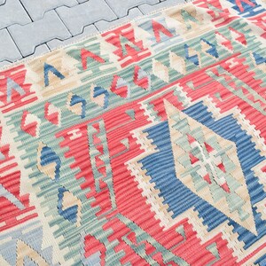 May include: A colorful woven rug with a geometric pattern in shades of red, blue, green, and beige. The rug has a traditional design with a central diamond shape.