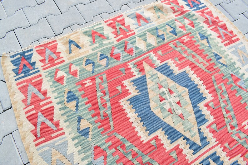 May include: A colorful woven rug with a geometric pattern in shades of red, blue, green, and beige. The rug has a traditional design with a central diamond shape.