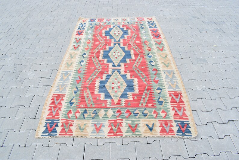May include: A traditional Turkish kilim rug with a geometric pattern in shades of red, blue, green, and beige. The rug has a rectangular shape and is woven with a variety of textures.