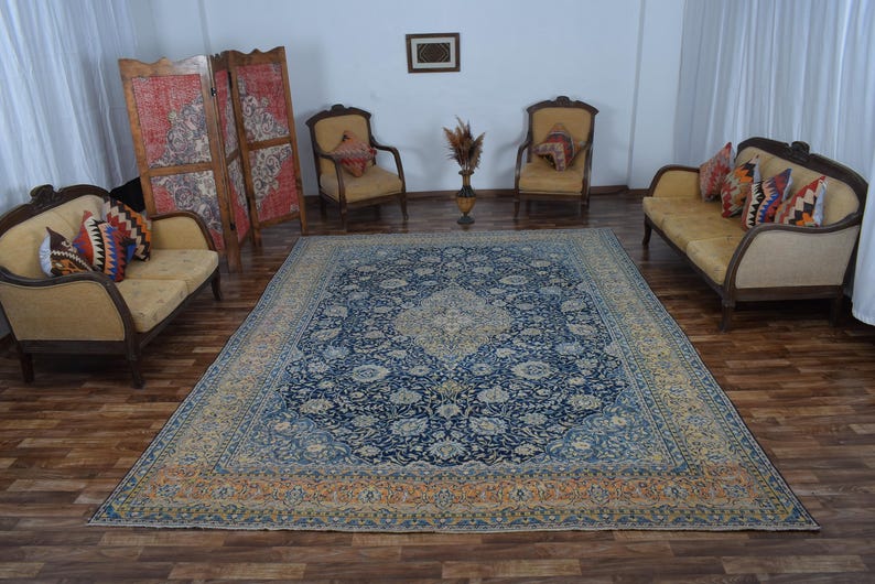 K&ouml;nnte beinhalten: Ein gro&szlig;er, rechteckiger, blau-beiger Perserteppich mit einem komplizierten Blumenmuster dominiert den Raum. Der Teppich ist von antiken M&ouml;beln umgeben, darunter zwei Sofas, zwei Sessel und ein Paravent. Der Raum hat eine warme, einladende Atmosph&auml;re.