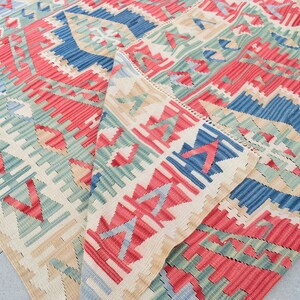 May include: A colorful woven rug with a geometric pattern in shades of red, blue, green, and beige. The rug is folded in half, revealing the intricate details of the design.