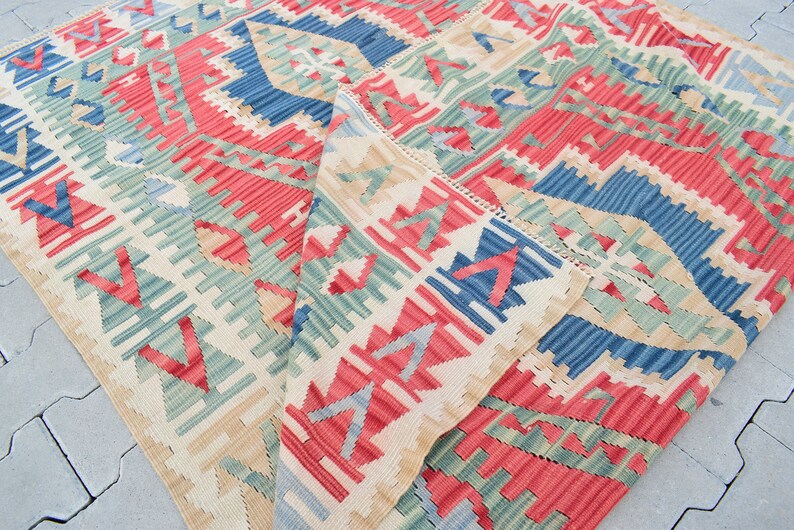May include: A colorful woven rug with a geometric pattern in shades of red, blue, green, and beige. The rug is folded in half, revealing the intricate details of the design.