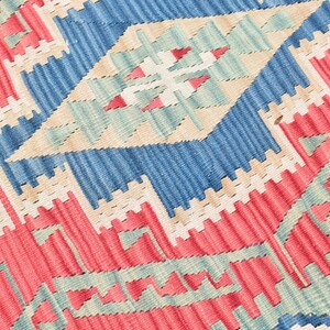 May include: Close-up of a woven rug with a geometric pattern in shades of red, blue, beige, and green.