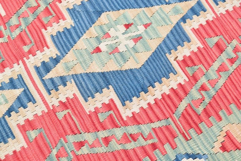 May include: Close-up of a woven rug with a geometric pattern in shades of red, blue, beige, and green.