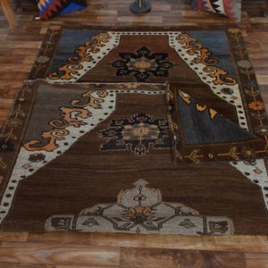 May include: A brown and blue area rug with detailed geometric patterns. The rug has a central medallion design with floral and geometric motifs in shades of brown, beige, and orange. The rug is placed on a wooden floor.