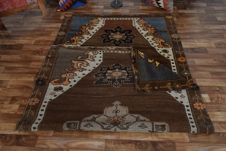 May include: A brown and blue area rug with detailed geometric patterns. The rug has a central medallion design with floral and geometric motifs in shades of brown, beige, and orange. The rug is placed on a wooden floor.