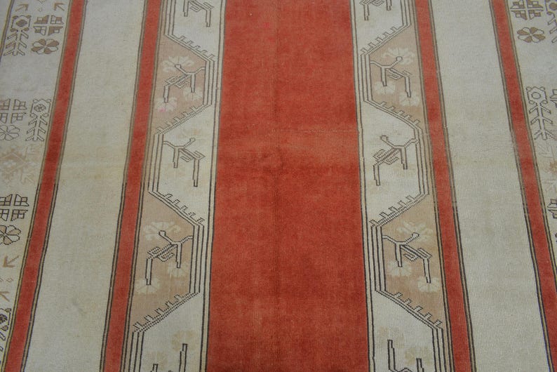 May include: A close-up view of a rug with a repeating pattern. The rug features vertical stripes in cream, coral, and a darker coral. The cream stripes have a repeating geometric design in a darker color.