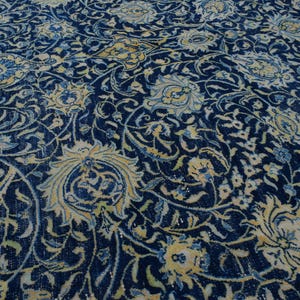 K&ouml;nnte beinhalten: Nahaufnahme eines detailreichen, verzierten Teppichs mit tiefblauem Hintergrund. Der Teppich zeigt ein komplexes Blumenmuster in Creme-, Hellblau- und Goldt&ouml;nen. Das Design ist aufwendig, mit wirbelnden Ranken und stilisierten Blumen.