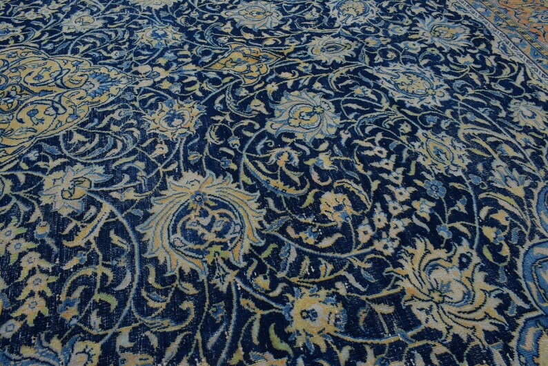K&ouml;nnte beinhalten: Nahaufnahme eines detailreichen, verzierten Teppichs mit tiefblauem Hintergrund. Der Teppich zeigt ein komplexes Blumenmuster in Creme-, Hellblau- und Goldt&ouml;nen. Das Design ist aufwendig, mit wirbelnden Ranken und stilisierten Blumen.