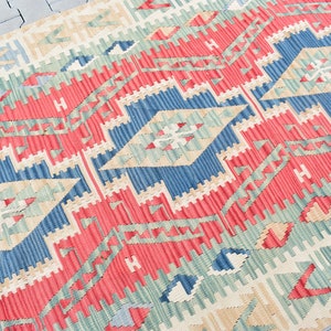 May include: A red, blue, and green patterned rug with a geometric design. The rug is woven with a traditional style and has a fringed edge.