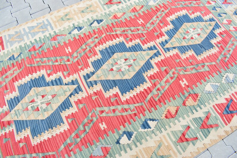 May include: A red, blue, and green patterned rug with a geometric design. The rug is woven with a traditional style and has a fringed edge.