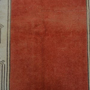 May include: Close-up of a vintage rug with a central rust-colored panel flanked by beige panels. The beige panels feature geometric patterns in black and brown, creating a striking contrast. The rug's texture is visible.