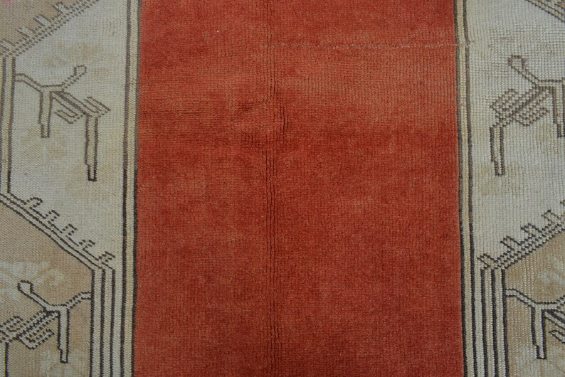 May include: Close-up of a vintage rug with a central rust-colored panel flanked by beige panels. The beige panels feature geometric patterns in black and brown, creating a striking contrast. The rug's texture is visible.