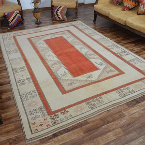 May include: A rectangular rug with a cream-colored field and a central orange rectangle. The rug features a border of orange and tan geometric patterns. The rug is placed on a hardwood floor.