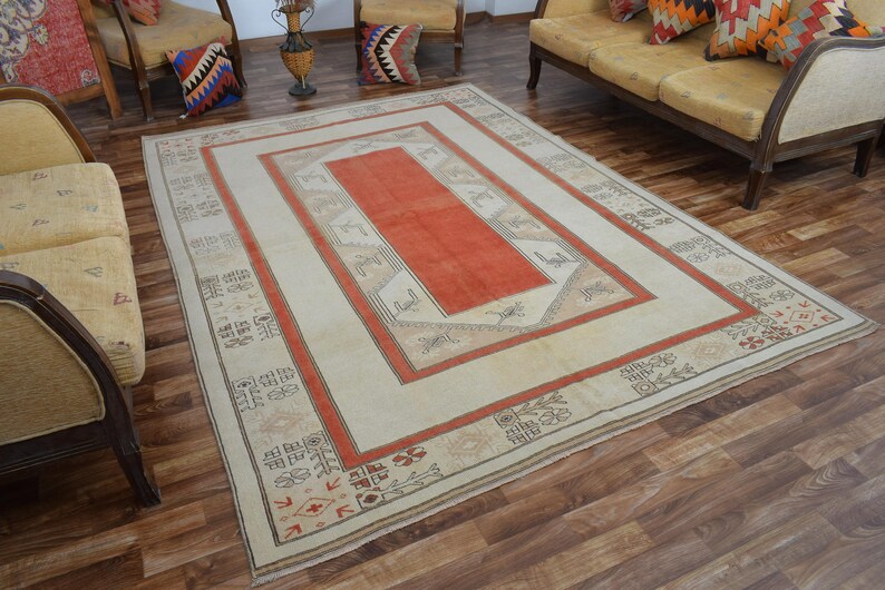 May include: A rectangular rug with a cream-colored field and a central orange rectangle. The rug features a border of orange and tan geometric patterns. The rug is placed on a hardwood floor.