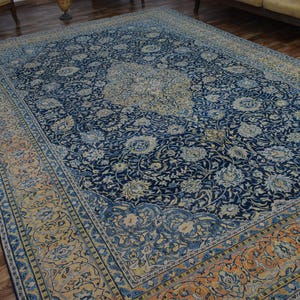 K&ouml;nnte beinhalten: Gro&szlig;er, rechteckiger persischer Teppich mit marineblauem Feld und aufwendigen Blumenmustern in Creme und Hellblau. Der Rand weist ein erg&auml;nzendes Design in Orange- und Cremet&ouml;nen auf, was einen klassischen, eleganten Look erzeugt.