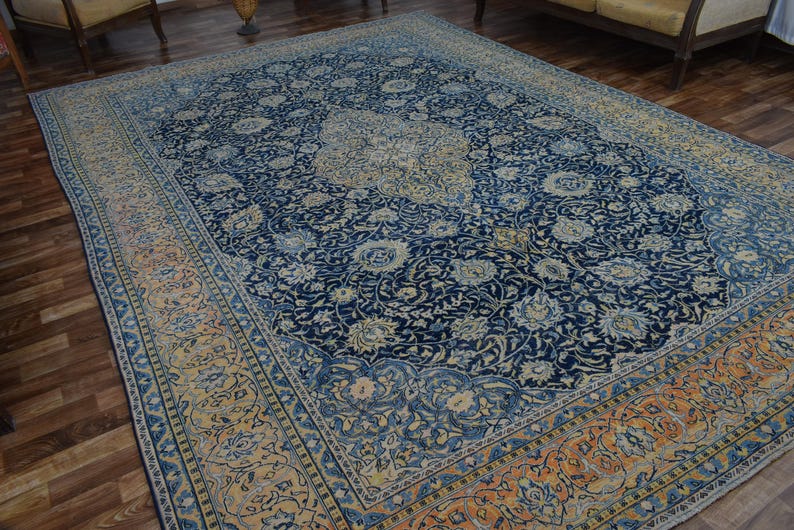 K&ouml;nnte beinhalten: Gro&szlig;er, rechteckiger persischer Teppich mit marineblauem Feld und aufwendigen Blumenmustern in Creme und Hellblau. Der Rand weist ein erg&auml;nzendes Design in Orange- und Cremet&ouml;nen auf, was einen klassischen, eleganten Look erzeugt.