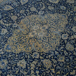 K&ouml;nnte beinhalten: Nahaufnahme eines persischen Teppichs mit marineblauem Hintergrund und aufwendigen Blumenmustern in Creme und Hellblau. Der Teppich hat ein zentrales Medaillon-Design.