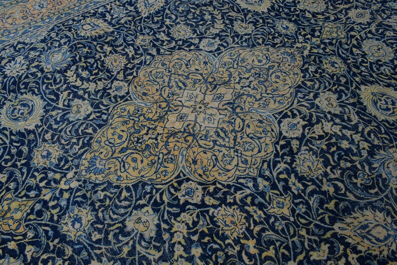 K&ouml;nnte beinhalten: Nahaufnahme eines persischen Teppichs mit marineblauem Hintergrund und aufwendigen Blumenmustern in Creme und Hellblau. Der Teppich hat ein zentrales Medaillon-Design.