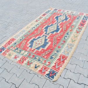 May include: A traditional Turkish kilim rug with a geometric pattern in shades of red, blue, green, and beige. The rug is woven with a flat weave and has a fringed edge.
