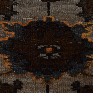 May include: Close-up of a section of a rug with a repeating pattern. The rug features a neutral beige background with dark brown and grey floral-like shapes. The edges of the shapes are outlined in orange.