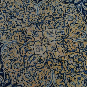 K&ouml;nnte beinhalten: Nahaufnahme eines verzierten Teppichs mit einem zentralen floralen Medaillon. Der Teppich hat einen marineblauen Rand und komplizierte Muster in Gold- und Blaut&ouml;nen. Das Design umfasst florale und arabeske Motive.