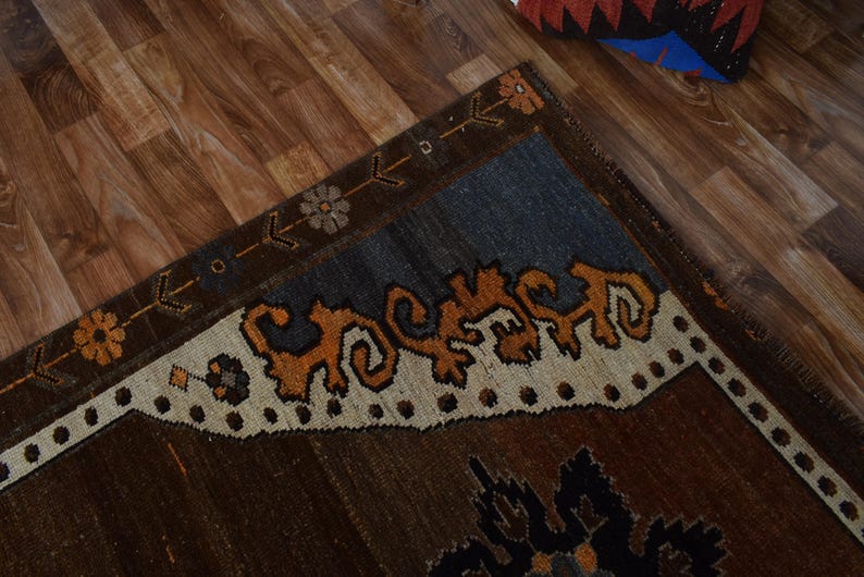 May include: A section of a brown rug with a blue and cream border. The rug features an intricate design with orange and brown patterns. The rug is placed on a wooden floor.