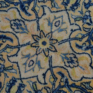 K&ouml;nnte beinhalten: Nahaufnahme eines Abschnitts eines antiken Teppichs mit floralem Muster. Der Teppich hat einen cremefarbenen Hintergrund mit aufwendigen Designs in Blau-, Gelb- und Gr&uuml;nt&ouml;nen. Das Muster umfasst stilisierte Blumen und Ranken.