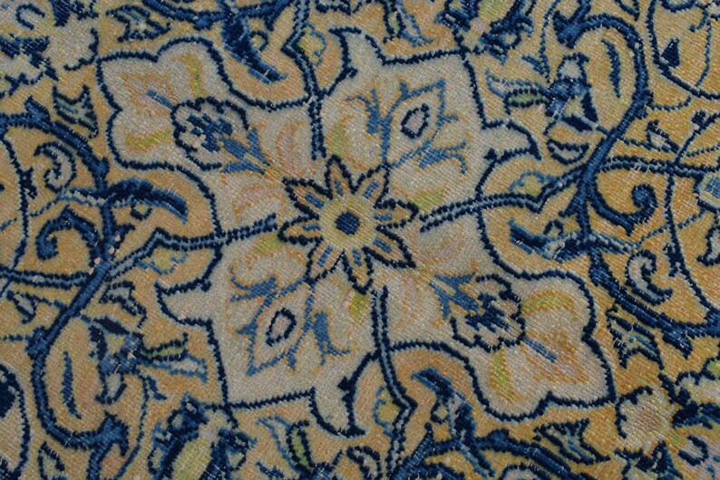 K&ouml;nnte beinhalten: Nahaufnahme eines Abschnitts eines antiken Teppichs mit floralem Muster. Der Teppich hat einen cremefarbenen Hintergrund mit aufwendigen Designs in Blau-, Gelb- und Gr&uuml;nt&ouml;nen. Das Muster umfasst stilisierte Blumen und Ranken.
