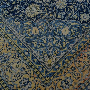 K&ouml;nnte beinhalten: Nahaufnahme eines Abschnitts eines verzierten Teppichs mit detailliertem Blumenmuster. Der Teppich hat ein marineblaues Mittelfeld mit gelben und blauen Blumenmotiven. Ein gelber Rand mit blauen Akzenten rahmt das Design ein und schafft einen klassischen, eleganten Look.