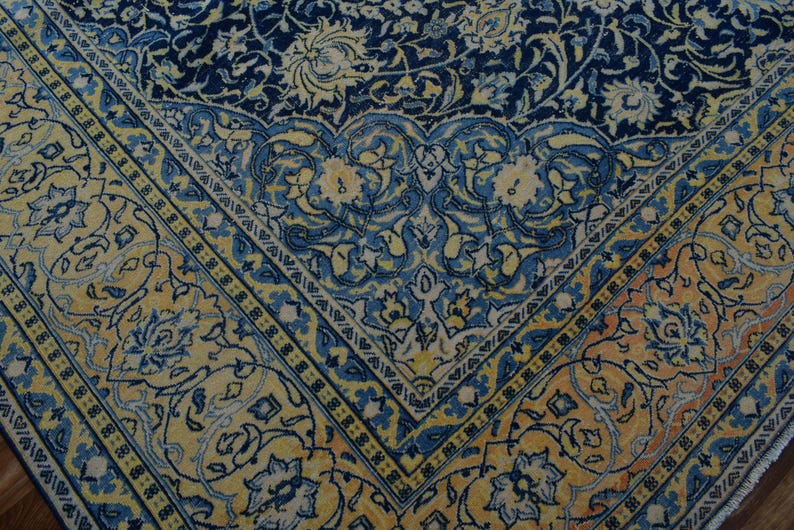 K&ouml;nnte beinhalten: Nahaufnahme eines Abschnitts eines verzierten Teppichs mit detailliertem Blumenmuster. Der Teppich hat ein marineblaues Mittelfeld mit gelben und blauen Blumenmotiven. Ein gelber Rand mit blauen Akzenten rahmt das Design ein und schafft einen klassischen, eleganten Look.