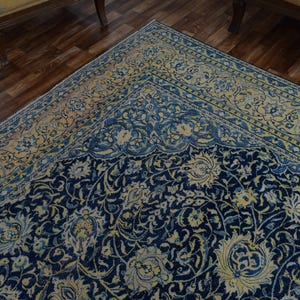 K&ouml;nnte beinhalten: Nahaufnahme eines marineblauen und cremefarbenen Teppichs. Der Teppich weist ein kompliziertes Blumenmuster mit einem cremefarbenen und hellblauen Rand auf. Der Teppich liegt auf einem dunklen Holzboden.