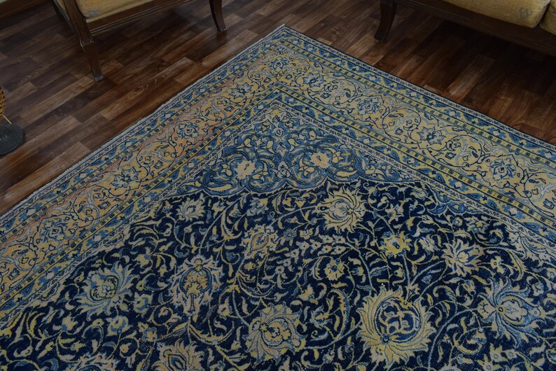 K&ouml;nnte beinhalten: Nahaufnahme eines marineblauen und cremefarbenen Teppichs. Der Teppich weist ein kompliziertes Blumenmuster mit einem cremefarbenen und hellblauen Rand auf. Der Teppich liegt auf einem dunklen Holzboden.
