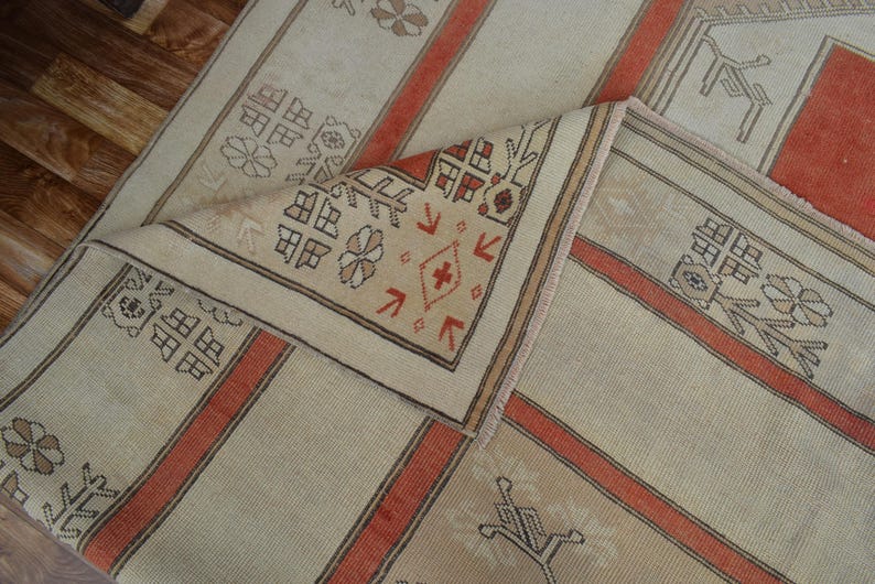 May include: Beige and orange patterned rug with a folded corner. The rug features a repeating geometric design with floral and linear elements. The color scheme includes beige, orange, and brown, creating a warm and inviting aesthetic. The rug is likely made of woven fabric.
