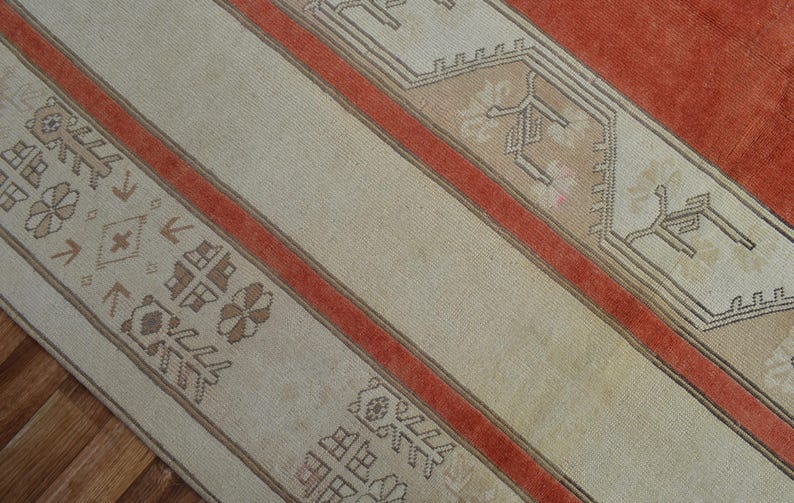 May include: Close-up of a section of a vintage rug with a cream-colored field and rust-colored stripes. The rug features geometric patterns in shades of brown and beige, creating a warm and inviting aesthetic. The rug is likely made of wool.