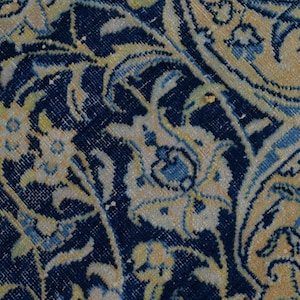 K&ouml;nnte beinhalten: Nahaufnahme eines Abschnitts eines persischen Teppichs mit detailliertem Blumenmuster. Der Teppich hat einen dunkelblauen Hintergrund mit cremefarbenen, hellblauen und gelben Blumen- und Rankenmotiven. Das Design ist aufwendig und traditionell und zeigt einen klassischen Teppichstil.