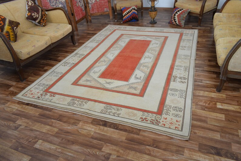 May include: Rectangular area rug with a central orange panel, framed by a cream border and a red outer border. The rug features geometric patterns and decorative elements, suitable for living room decor.