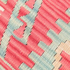 May include: Close-up of a woven rug with a geometric pattern in shades of red, blue, and beige.