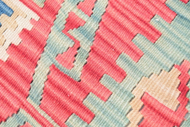 May include: Close-up of a woven rug with a geometric pattern in shades of red, blue, and beige.