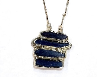 Puede incluir: Un collar de cadena dorada con un colgante de piedra azul en capas.