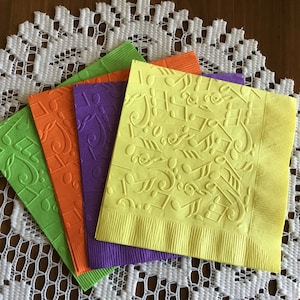 May include: Four paper napkins with a musical note design. The napkins are in shades of green, orange, purple, and yellow.