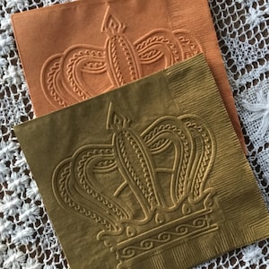 May include: Two paper napkins with an embossed crown design. The top napkin is orange and the bottom napkin is gold.