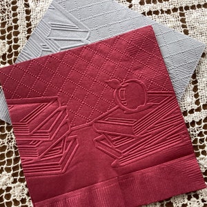 May include: Two red and gray paper napkins with an embossed design. The red napkin has a design of an apple and books. The gray napkin has a diamond pattern.